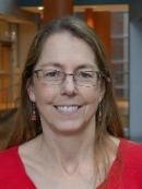 A smiling person with long dark blond hair, glasses, and a red top